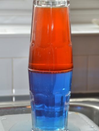 Two glasses on top of each other filled with water, food colouring and different amount of salt. One colour floats on top of the other.