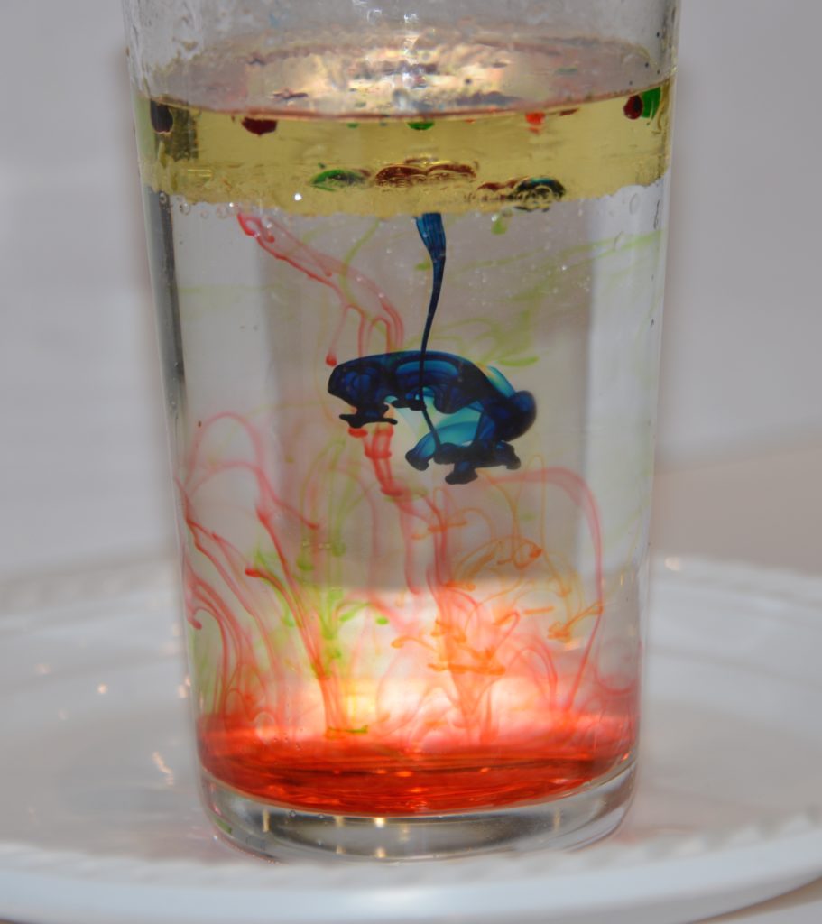 oil, water and food colouring in a glass. The food colouring is creating swirls of colour through the water.