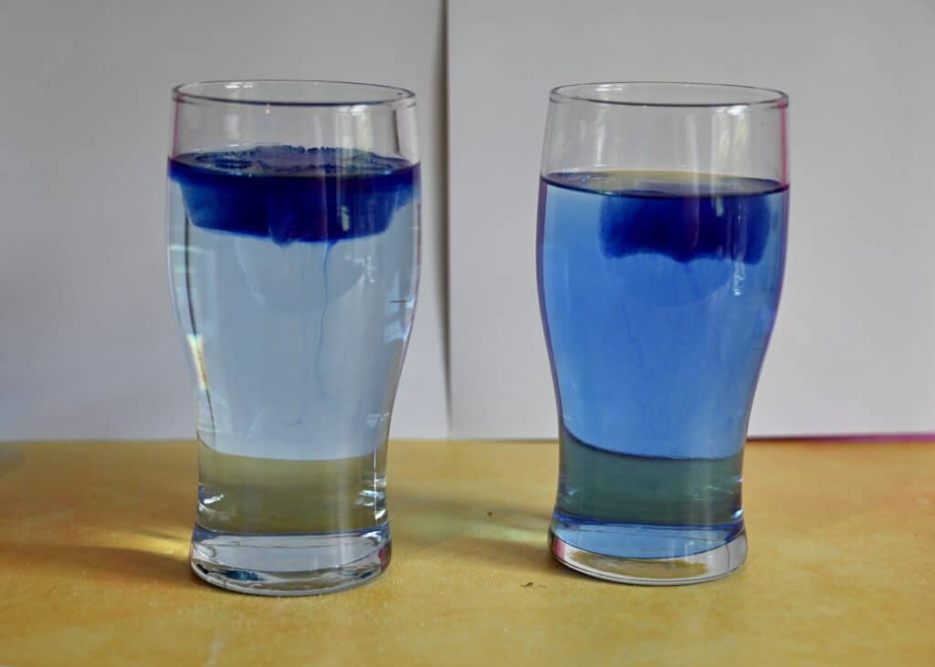 two glasses filled with water. One contains salt and both contain a blue ice cube