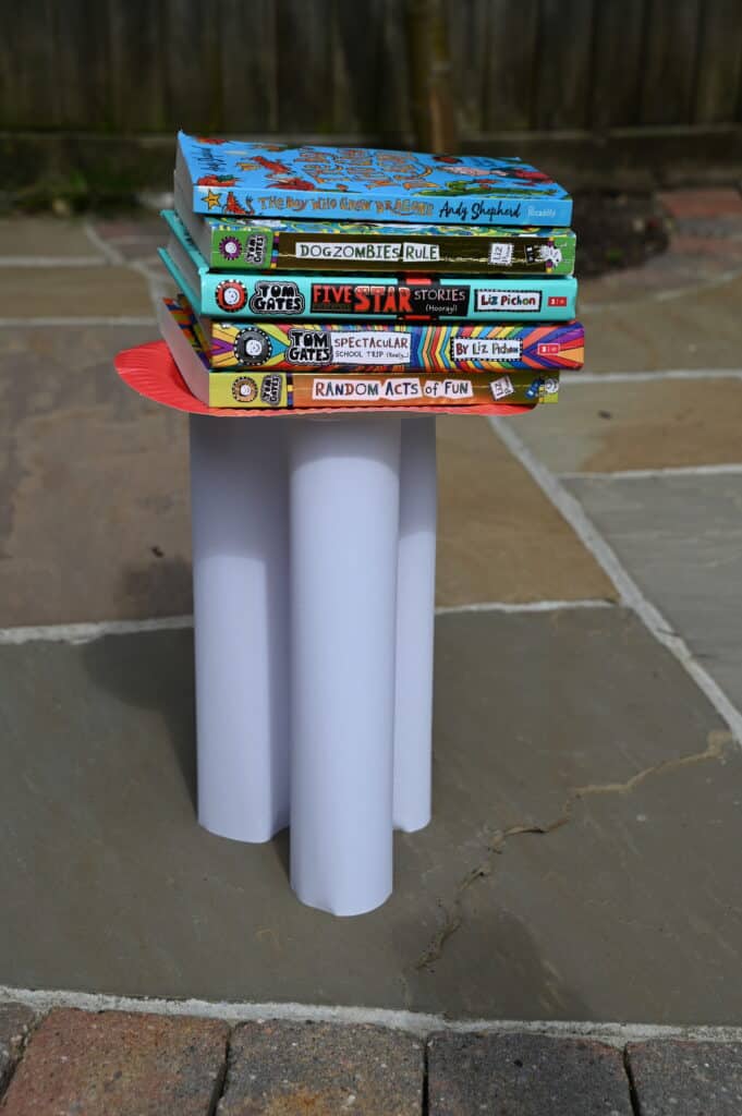 3 circular columns with a paper plate balanced on the top and a stack of books on top of that.